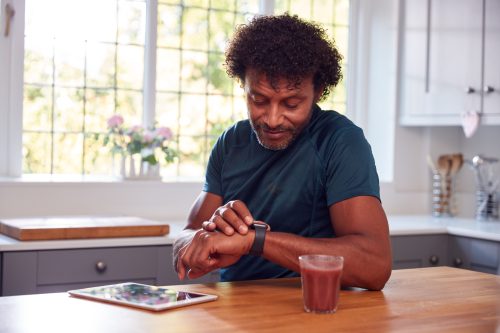 Bărbat matur care poartă haine de fitness acasă, înregistrând activitatea de la ceas inteligent la tabletă digitală