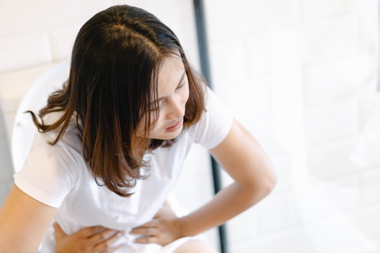 Woman sitting down, in stomach pain.