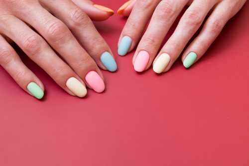 Colored matte manicure on female hands on a red background with copy space