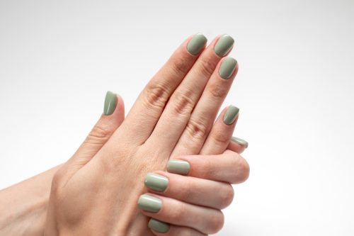 Mâna de femeie frumoasă cu unghii verzi.  Manichiură proaspătă izolată pe fundal alb.