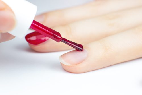 Woman applies red nail polish. Girl making a manicure. Salon procedures at home. Beautiful hands and nails. Close up, macro photo.
