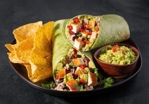 Chicken burrito in a spinach tortilla with corn chips and guacamole