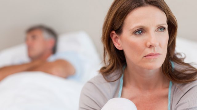 Sad woman on bed with her husband in the background