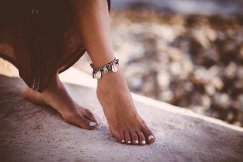 Cận cảnh bàn chân của người phụ nữ trẻ theo phong cách bohemian đeo vòng tay bằng bạc và ngọc lam ở bãi biển