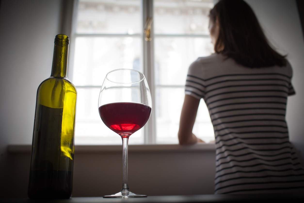 Woman at the window with glass of wine in the foreground.