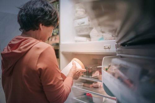 Femeie în vârstă care deschide frigiderul scoțând înghețată congelată noaptea în bucătărie