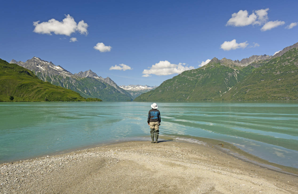 A hiker standing on the shore of a lake in Lake Clark National Park