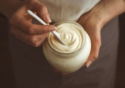 Glass jar of mayonnaise and a white spoon in hand.