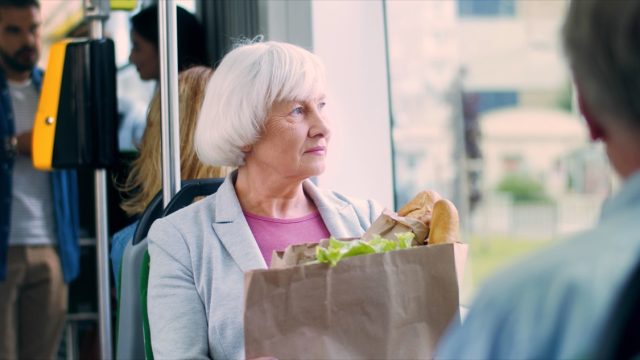 Portrait of pretty gray-haired Caucasian old woman with a big packet of vegetables and other food going home in public transportation.