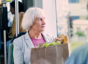 Portrait of pretty gray-haired Caucasian old woman with a big packet of vegetables and other food going home in public transportation.