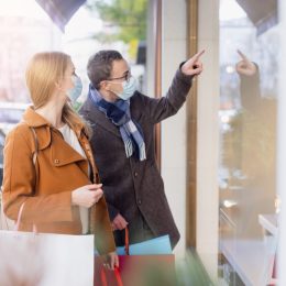 Couple doing shopping during partial lockdown standing in front of shop window with mask
