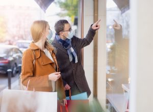 Couple doing shopping during partial lockdown standing in front of shop window with mask