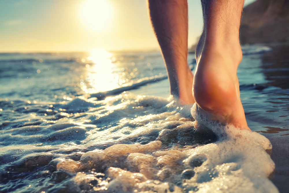 Close up of a person's feet as they walk into the water at the beach