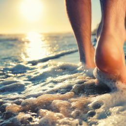 Close up of a person's feet as they walk into the water at the beach