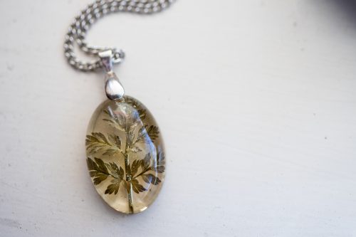 Un colier de argint cu un farmec de rășină și o frunză verde uscată în interior