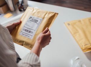 Hands of an unrecognisable small business owner holding a yellow envelope with shipping details before dispatching it