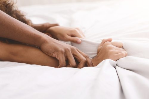 close up of man and woman's hands grasping sheets in bed