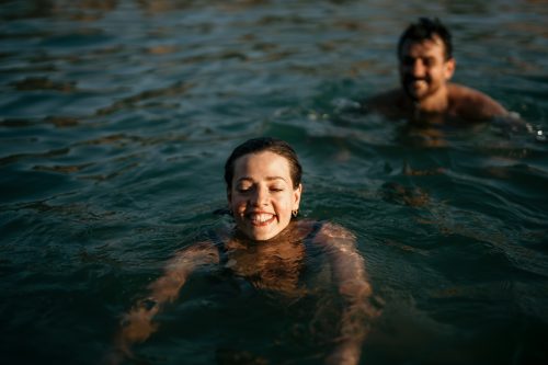 Young happy couple having fun while swimming in the sea. A woman is splashing her boyfriend and they are both laughing.