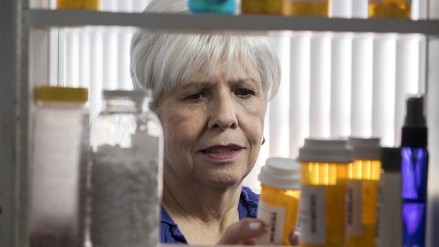 A senior woman checking bottles of medicine in a cabinet