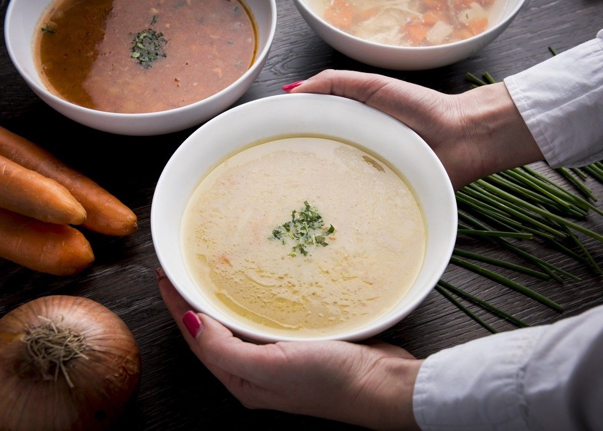 Women hands in a white shirt holding a bowl of cream soup