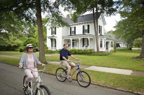 A couple riding bikes past a big historic white house in Madison, Georgia