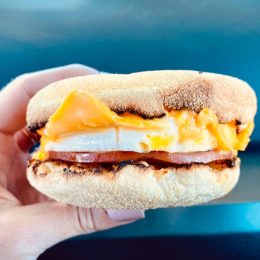 Person Holding Breakfast Sandwich with Egg Ham Bacon and Cheese on Toasted English Muffin