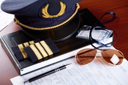 Professional airline pilot hat and id holder with epaulets and sun glasses laying on log book and flight plan.