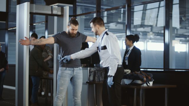 A TSA agent uses a metal detector to scan a male passenger at an airport security checkpoint