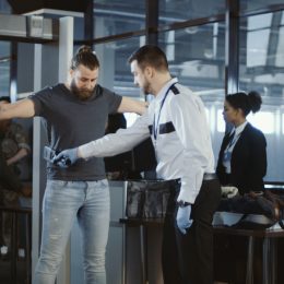 A TSA agent uses a metal detector to scan a male passenger at an airport security checkpoint