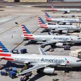 Five American Airlines planes sitting at their gates and one plane taxiing on the runway at an airport