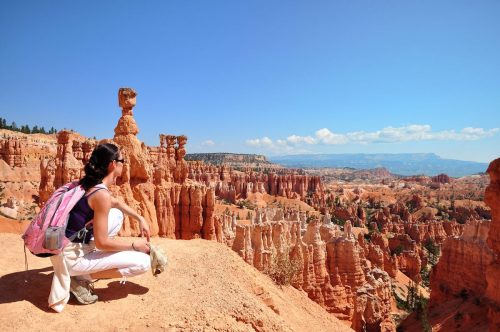 A young woman crouching down at overlook at Bryce Canyon National Park in Utah with all the red-rock hoodoos in the background