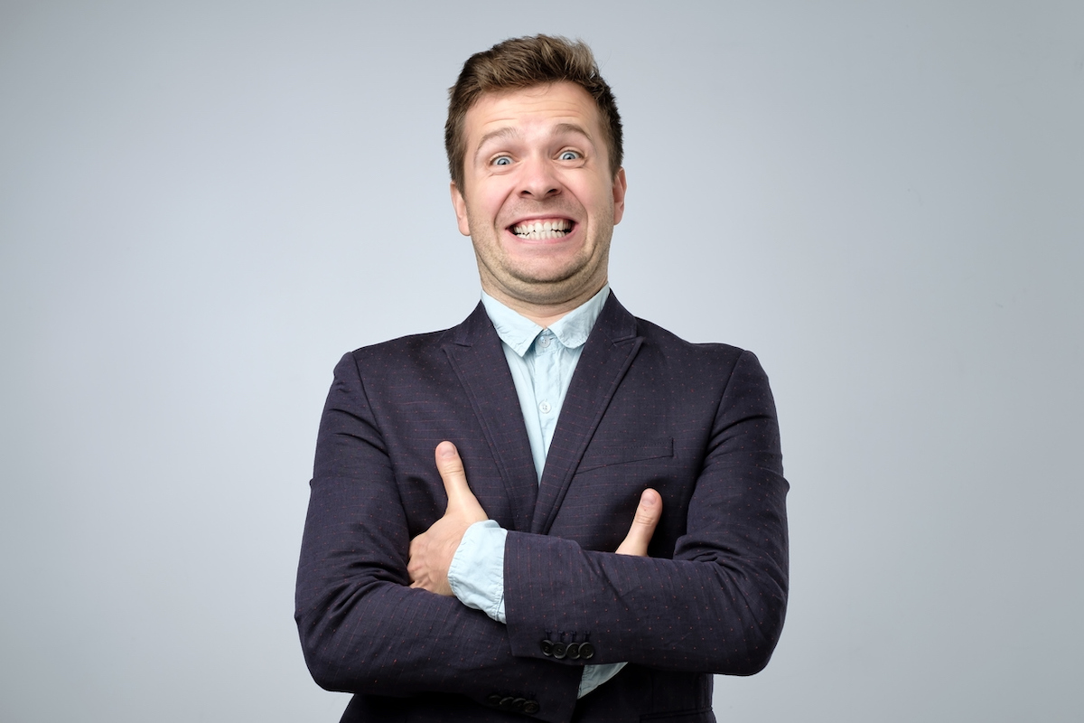 A businessman in a navy blue suit gives a fake smile.