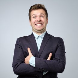 A businessman in a navy blue suit gives a fake smile.