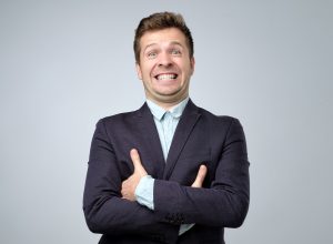 A businessman in a navy blue suit gives a fake smile.