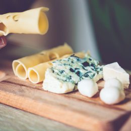 A closeup of a someone eating from a cheese board with a variety of items