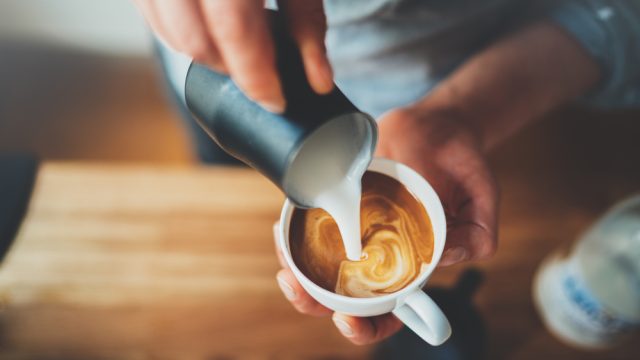 Closeup of a barista pouring milk into a coffee drink