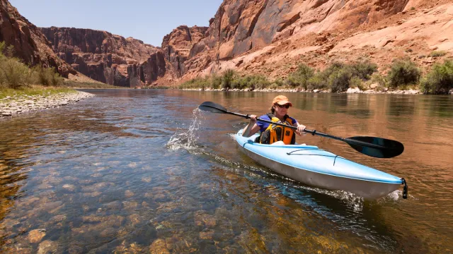 A woman kayaking the Colorado River (Between Lees Ferry and Glen Canyon Dam). Red/organe stones line the water