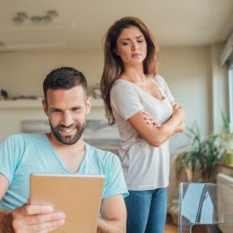 Young woman jealously looking at the smiling man using digital tablet