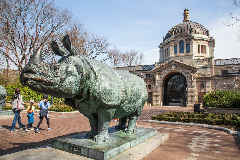A family walking through the Bronx Zoo near a statue of a rhinoceros