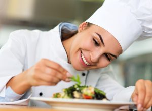 Close up of a female chef in a chef's hat and coat plating a salad