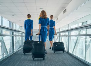 A trio of flight attendants walking down the jetway with their baggage