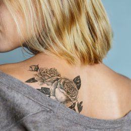 Close up of a young blonde woman's back with a large rose tattoo.