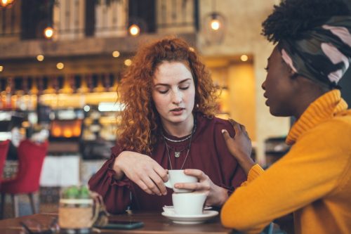 A young woman talks to a friend about her problem at the coffee shop.  The friend is supportive and understanding.