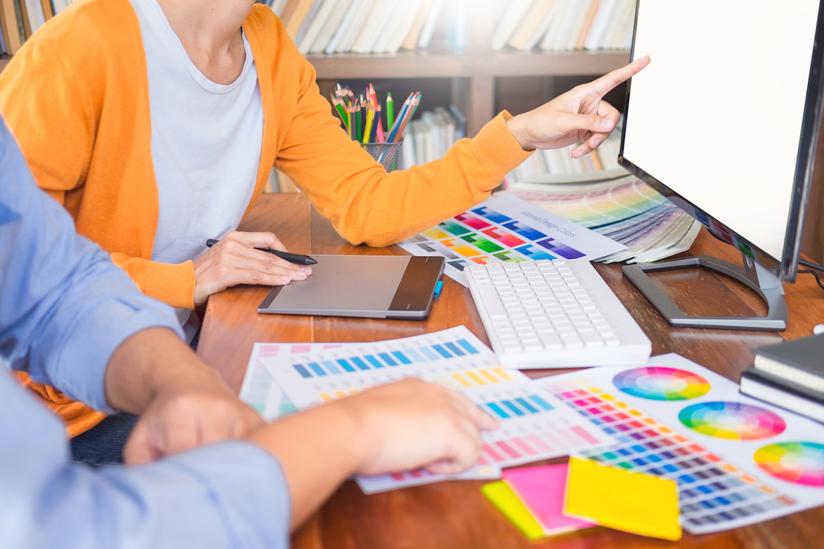 A graphic designer at her computer with a client showing him color samples
