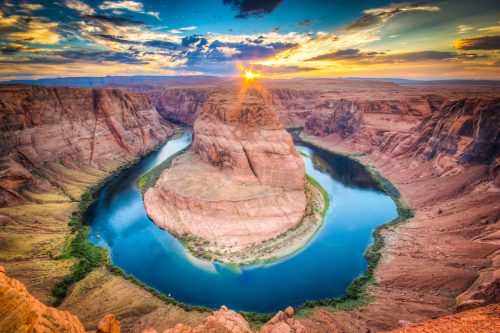 Sunset at Horseshoe Bend, part of the Colorado River in Arizona. Clear blue waters are surrounded by red and orange rock formations.