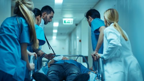 Emergency Department: Doctors, Nurses and Surgeons Move Seriously Injured Patient Lying on a Stretcher Through Hospital Corridors