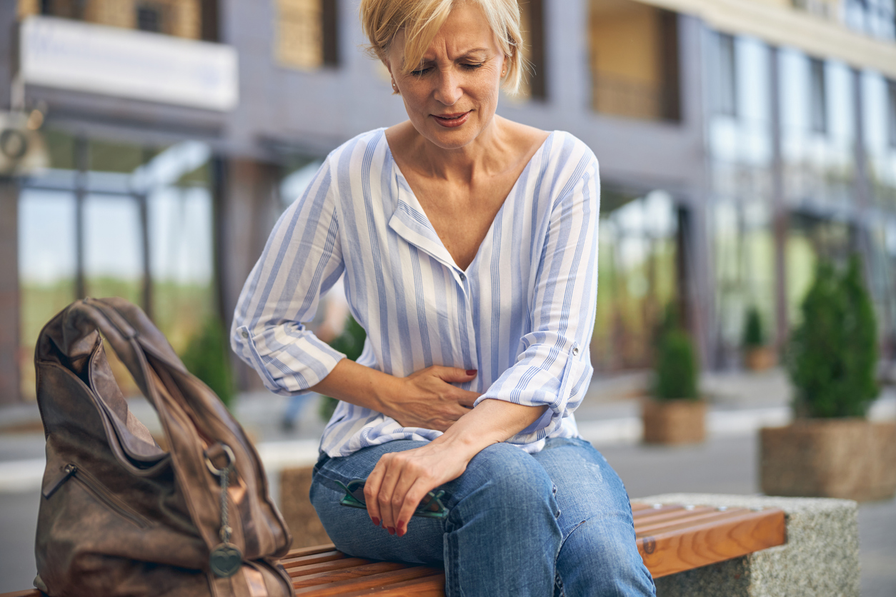 Woman sitting on a bench suffering from abdominal pain.