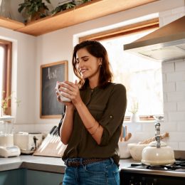 young woman having a cup of coffee while standing in her kitchen at home