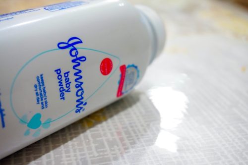 Close up image of white bottle of Johnson's baby powder isolated on table. Focus on text Johnson's at center of bottle; other in blur.