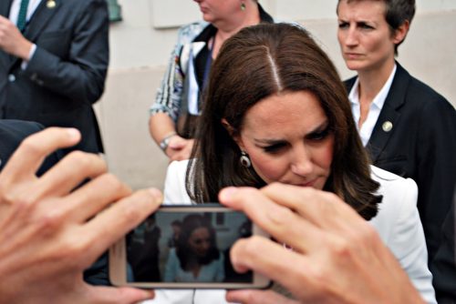Kate Middleton greeting crowds in Warsaw. People cheering for Kate and William. People are taking photos. Blurred background.